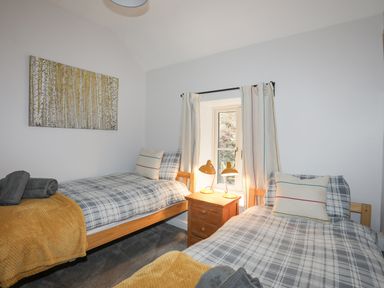 A bedroom with two single beds with plaid bedding and a wooden nightstand with two lamps at Glyn Awel Nant Gwynant near Beddgelert