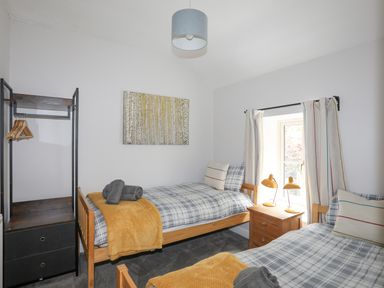 A bedroom with two single beds a wooden nightstand with lamps and a clothing rack at Glyn Awel in Nant Gwynant near Beddgelert