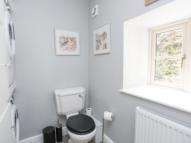 A small bathroom with a toilet a window and stacked washer and dryer at Glyn Awel Nant Gwynant near Beddgelert