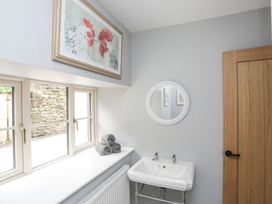 A bathroom with a white sink a round mirror gray towels on a windowsill and a wooden door at Glyn Awel in Nant Gwynant near Beddgelert