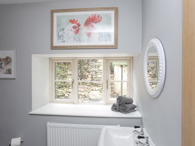 A bathroom with a window showing a stone wall and towels on the windowsill at Glyn Awel in Nant Gwynant near Beddgelert