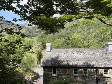 A house with a stone roof and trees in the foreground at Glyn Awel, Nant Gwynant near Beddgelert