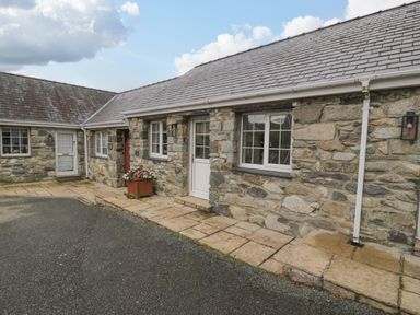 Exterior view of a stone house with two windows, two doors, a flower planter, and a paved walkway at Bwythyn Yr Wyddfa in Llanberis