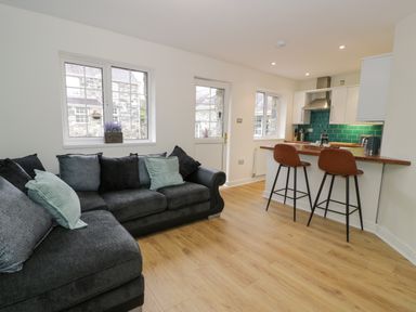 A living room with a sectional sofa and a kitchen with stools and teal tile backsplash at Bwythyn Yr Wyddfa in Llanberis