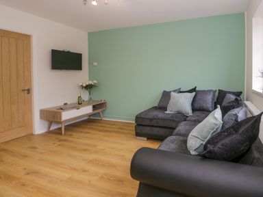 A living room with a grey sectional sofa and a wooden media console with a wall-mounted TV at Bwythyn Yr Wyddfa in Llanberis