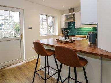 A kitchen with a wooden countertop breakfast bar with brown chairs and green tiled backsplash at Bwythyn Yr Wyddfa in Llanberis