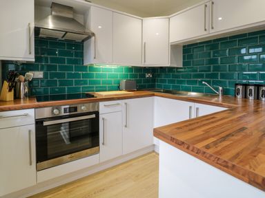 A kitchen with wooden countertops white cabinets teal tile backsplash oven and sink at Bwthyn Yr Wyddfa in Llanberis