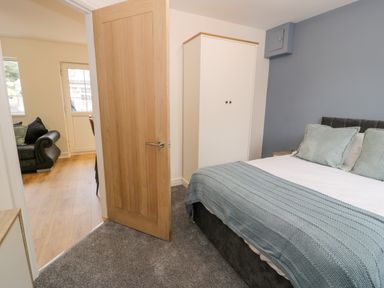 A bedroom with a bed with pillows and a blanket a white wardrobe an open wooden door and a view of a living room with a sofa at Bwythyn Yr Wyddfa in Llanberis