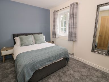 A bedroom with a bed two pillows a blue throw two side tables a window with curtains a wall mirror and a closed wooden door at Bwythyn Yr Wyddfa in Llanberis