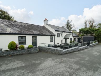 An outdoor seating area with tables and chairs outside a building with a tiled roof and sign reading The Little Tavern at Bwythyn Yr Wyddfa in Llanberis