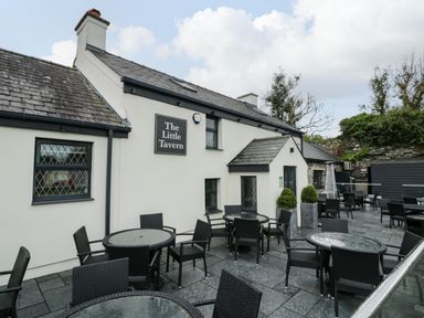 Outdoor seating area with glass tables and black chairs next to a building with a sign The Little Tavern at Bwythyn Yr Wyddfa in Llanberis