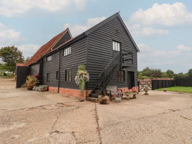 An outdoor view of a black barn with steps and flower pots at The Cow Shed in Chediston near Halesworth