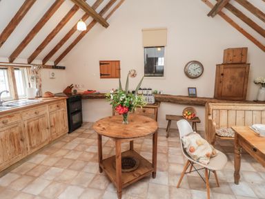 A kitchen with a round table and wooden cabinets at The Cow Shed in Chediston near Halesworth