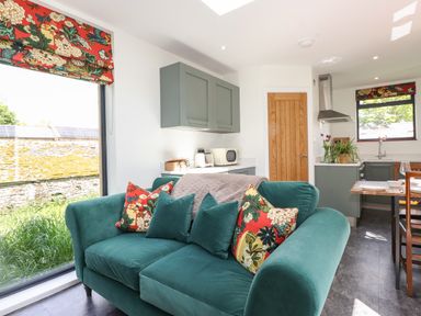 A kitchen and living area with a green sofa pillows and floral blinds at Brow Wood Cabin in Ullswater