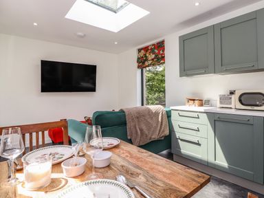 A dining table set with plates and glasses near a green sofa and kitchen cabinets with appliances at Brow Wood Cabin in Ullswater