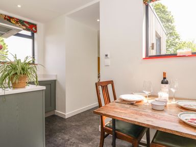 A dining area with a wooden table set for four near windows and a kitchen counter with a potted plant at Brow Wood Cabin in Ullswater