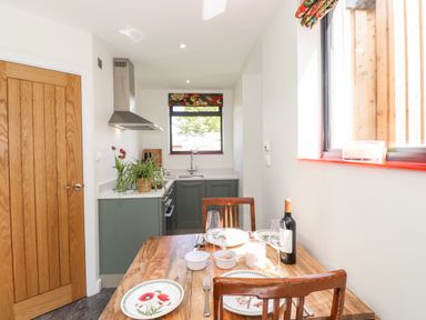 A kitchen with green cabinets and a wooden dining table set with plates and wine at Brow Wood Cabin in Ullswater