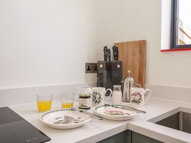 A kitchen corner with plates cups cutlery a jar of jam and glasses of juice at Brow Wood Cabin in Ullswater