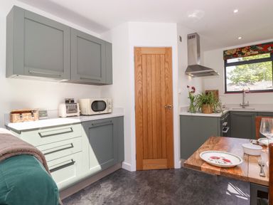 A kitchen with green cabinets a wooden door a microwave and toaster on the counter and a dining table with plates at Brow Wood Cabin Ullswater