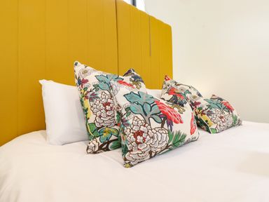 A bed with white sheets pillows and floral cushions against a yellow headboard at Brow Wood Cabin in Ullswater