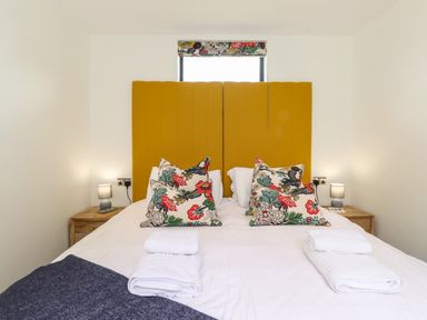 A bedroom with a double bed with yellow headboard and floral pillows at Brow Wood Cabin in Ullswater