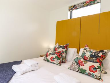 A bedroom with towels on white bed and patterned pillows with yellow headboard at Brow Wood Cabin in Ullswater