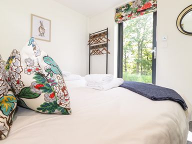 A bedroom with a bed floral cushions folded towels and a coat rack near a window at Brow Wood Cabin in Ullswater