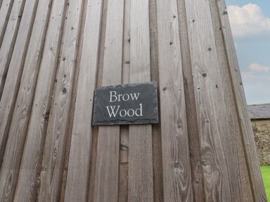 A wooden wall with a black sign that reads Brow Wood at Brow Wood Cabin in Ullswater