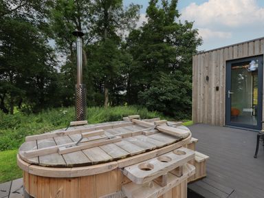 An outdoor wooden hot tub with a cover next to a wooden cabin with a glass door at Brow Wood Cabin in Ullswater