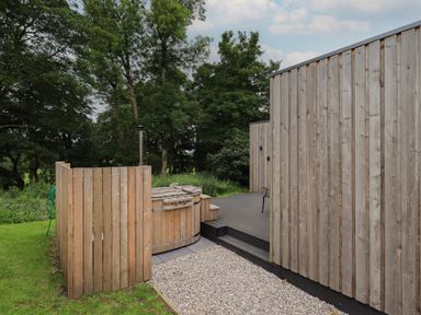 An outdoor area with a wooden hot tub surrounded by trees at Brow Wood Cabin in Ullswater
