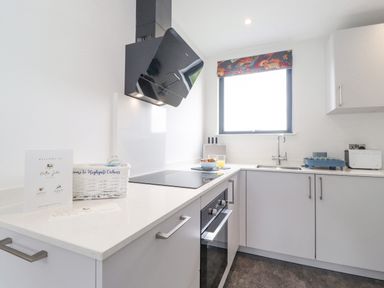 A kitchen with white cabinets an electric cooktop and oven a window above a sink a toaster and a dish rack on the counter at Bluebell Cabin in Ullswater