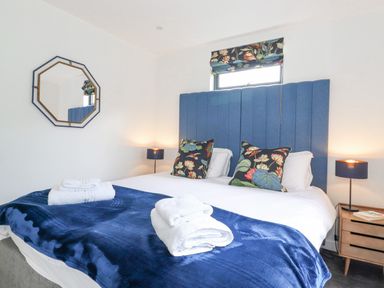 A bedroom with a double bed with blue headboard and floral cushions at Bluebell Cabin in Ullswater