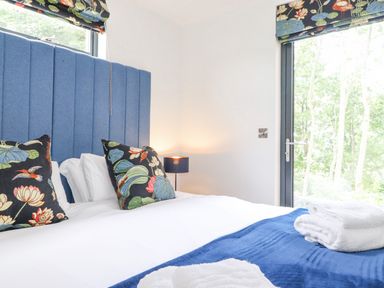 A bedroom with a blue headboard floral cushions white bed linens and a blue blanket at Bluebell Cabin in Ullswater