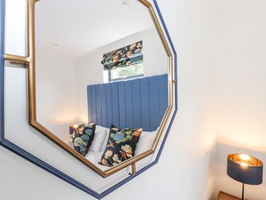 A reflection of a bedroom with a blue upholstered headboard floral pillows window and a lamp at Bluebell Cabin in Ullswater