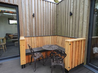 An outdoor corner seating area with wooden benches and a small round metal table with two metal chairs at Bluebell Cabin in Ullswater