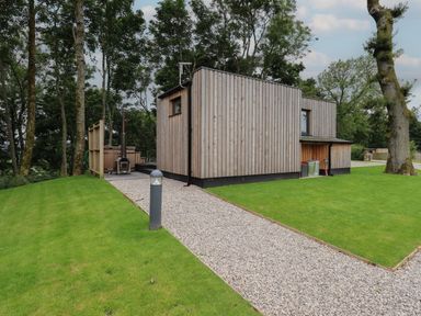 A wooden cabin with a gravel path leading to it surrounded by grass and trees at Bluebell Cabin in Ullswater