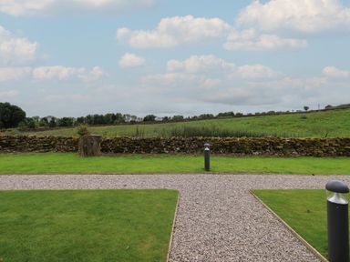 A gravel path crossing green grass with stone wall and fields beyond at Bluebell Cabin in Ullswater