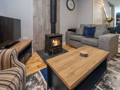 A living room with a wood-burning stove a grey sofa blue cushion a striped armchair wooden coffee table and a television at The Dollhouse in Cayton Bay