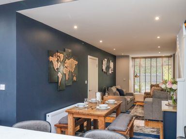 A dining and living area with a wooden table and benches a sofa and armchair and wall art at The Dollhouse in Cayton Bay