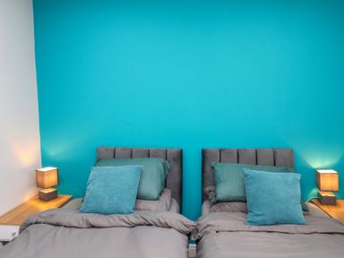 A bedroom with two single beds with grey bedding and blue pillows and bedside tables with lamps at The Dollhouse in Cayton Bay