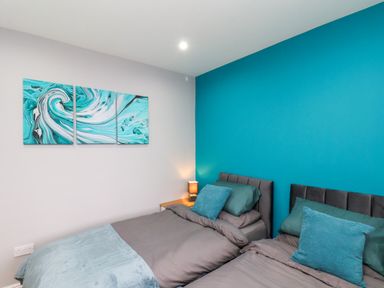 A bedroom with two single beds side by side a nightstand with a lamp and three abstract paintings on the wall at The Dollhouse in Cayton Bay