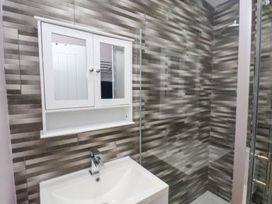 A bathroom with a white sink cabinet a mirrored wall cabinet and a shower area with patterned tiles at The Dollhouse in Cayton Bay