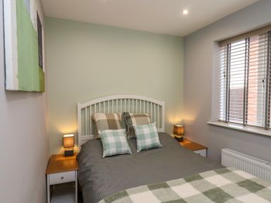 A bedroom with a bed with checkered pillows and blankets bedside tables with lamps and a window with blinds at The Dollhouse in Cayton Bay