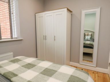 A bedroom with a bed covered by a checkered blanket a white wardrobe and a full-length mirror on the wall at The Dollhouse in Cayton Bay