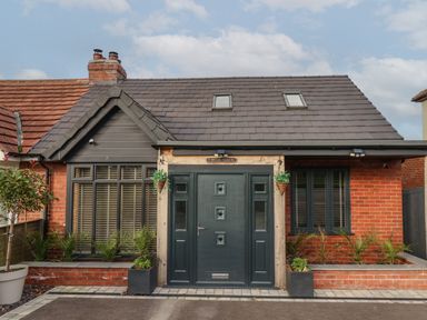 The front exterior of a brick house with a dark door two windows and plants at The Dollhouse in Cayton Bay