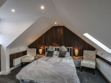 A bedroom with a bed bedside tables lamps and two chairs under a sloped ceiling at The Dollhouse in Cayton Bay