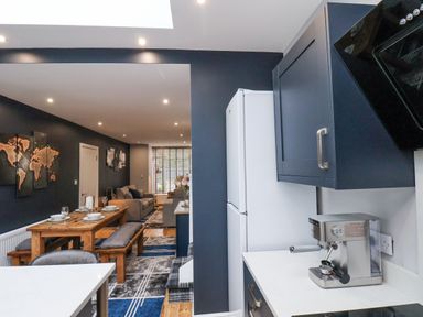 An open kitchen and dining area with wooden table set with dishes and a living room with sofas and wall art at The Dollhouse in Cayton Bay
