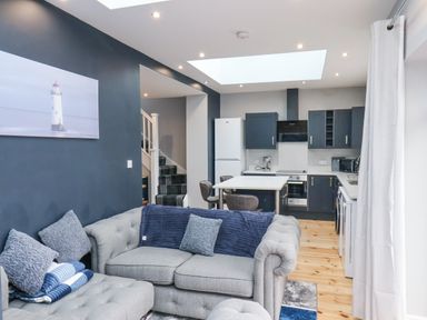 A living room and kitchen area with grey sofas pillows and a table at The Dollhouse in Cayton Bay