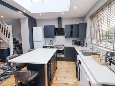 A kitchen with an island and bar stools with appliances and a window at The Dollhouse in Cayton Bay