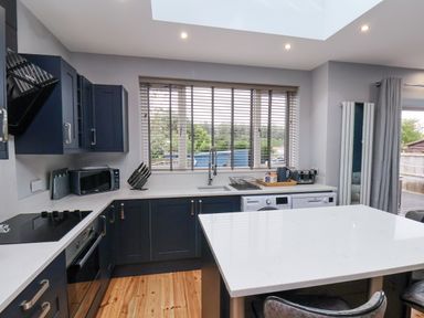 A kitchen with dark cabinets a white countertop a stove a microwave a sink a dishwasher and a window with blinds at The Dollhouse in Cayton Bay